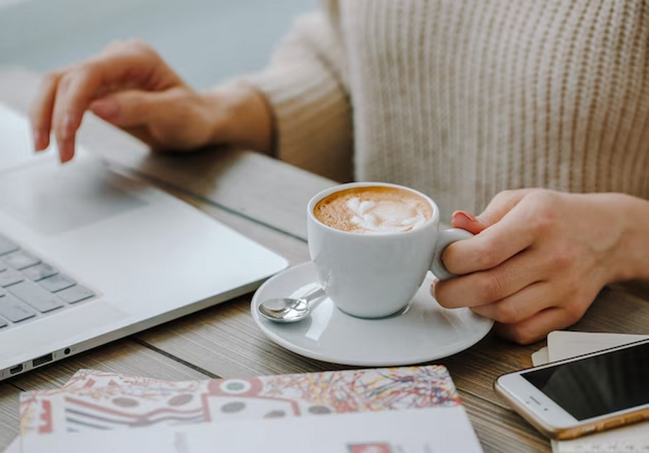 Woman holding coffee while working on a laptop.