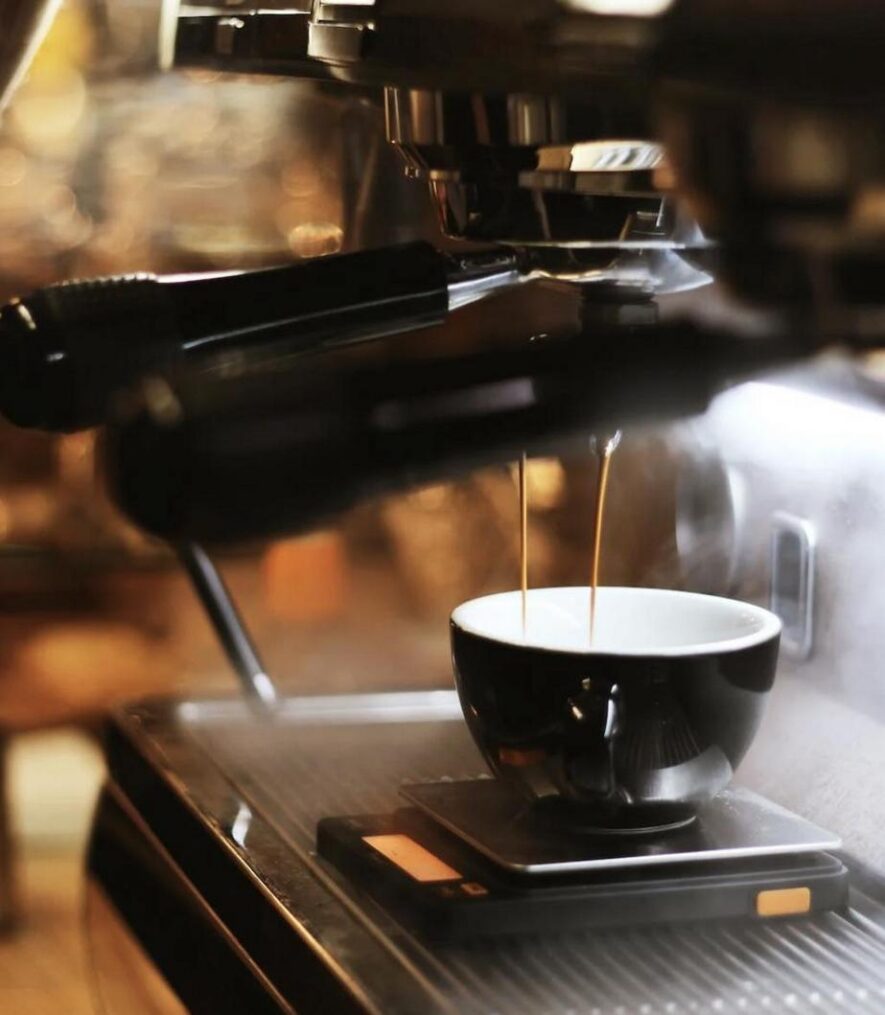 Espresso being brewed into a black ceramic cup on a digital scale